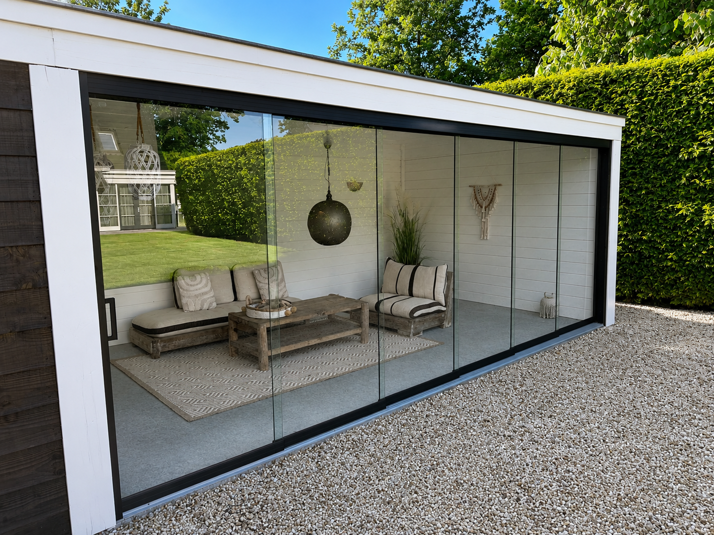 Glazen schuifwand in moderne tuinkamer met witte omkadering en zwarte profielen